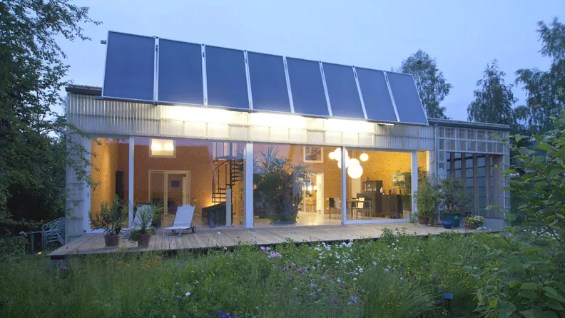 energie.spar.haus in Frauenau in der Dämmerung, Solarkollektoren auf dem Dach, Wiese davor