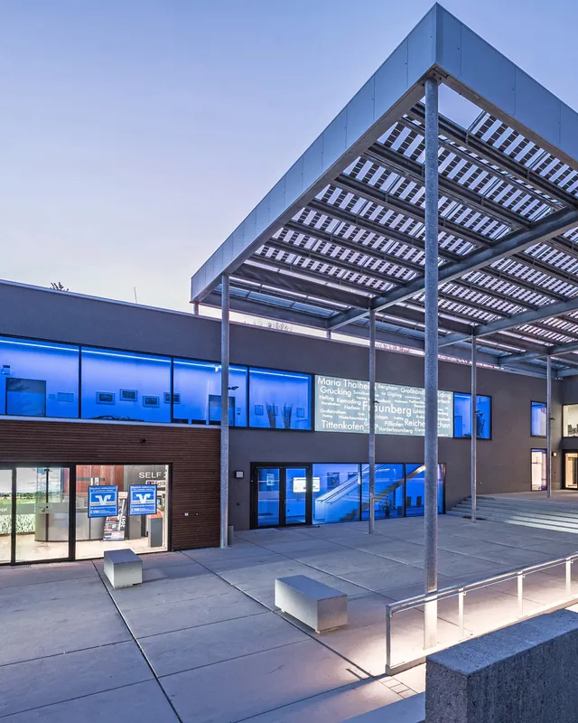 Gemeindezentrum Fraunberg in der Abenddämmerung: Vorplatz unter einem Dach aus transparenten Photovoltaikmodulen