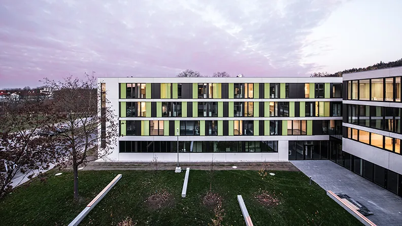 Jugendwohnheim Landshut am Abend: Sichtbetonfassade mit gelbgrünen Schiebeläden um einen Innenhof