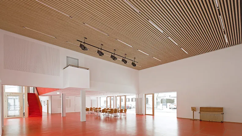 Saal im Pfarrheim St. Wolfgang mit Holzlamellendecke, roter Treppe und rotem Boden